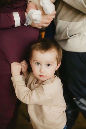 A young child in beige clothing reaches up while standing between adults.