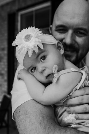 Sweet black and white portrait of a baby wearing a white flower headband being held close by an adult.