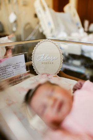 A decorative name sign reading 'Aleine Noelle' sits on a mirrored surface in a nursery setting.