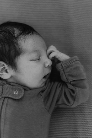 A sleeping baby in a gray sweater lying in black and white profile view in a series of similar photos.