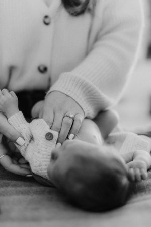 A close-up black and white photo of hands changing a baby's diaper, with a wedding ring visible on one finger.