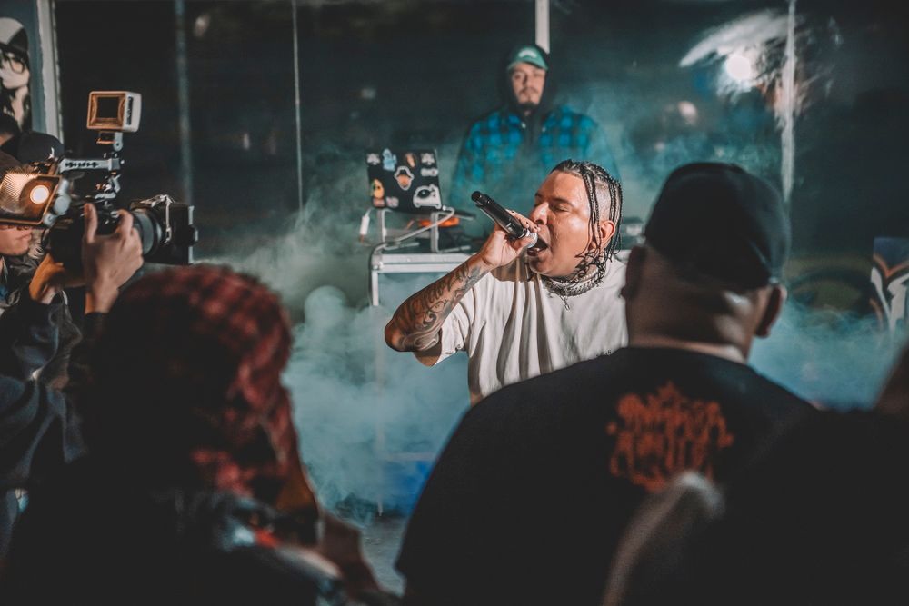 A performer on stage captured in smoky atmosphere with audience and camera crew silhouettes in the foreground.