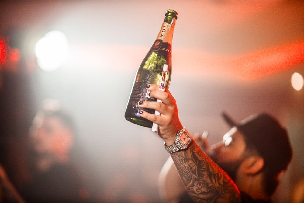 Hand holding champagne bottle in nightclub with red lighting effects.
