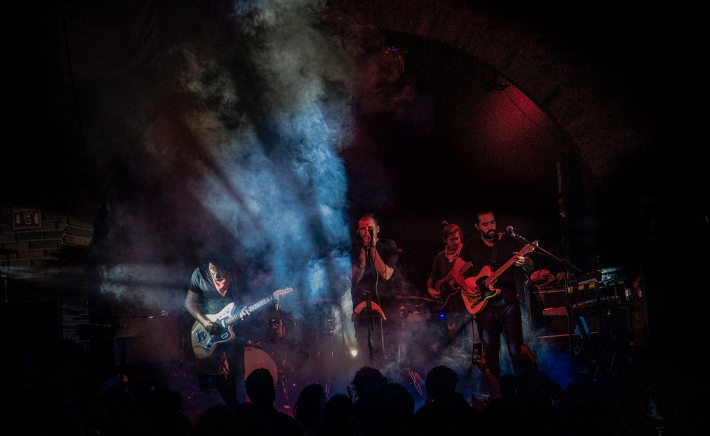 Rock band performs on dark stage with dramatic blue and red lighting effects.