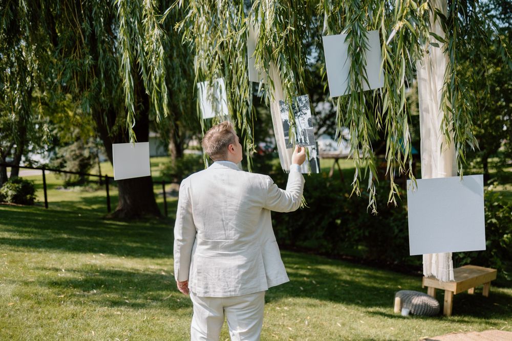 White-clad figure examining blank pages hanging from willow tree branches in an outdoor garden setting.