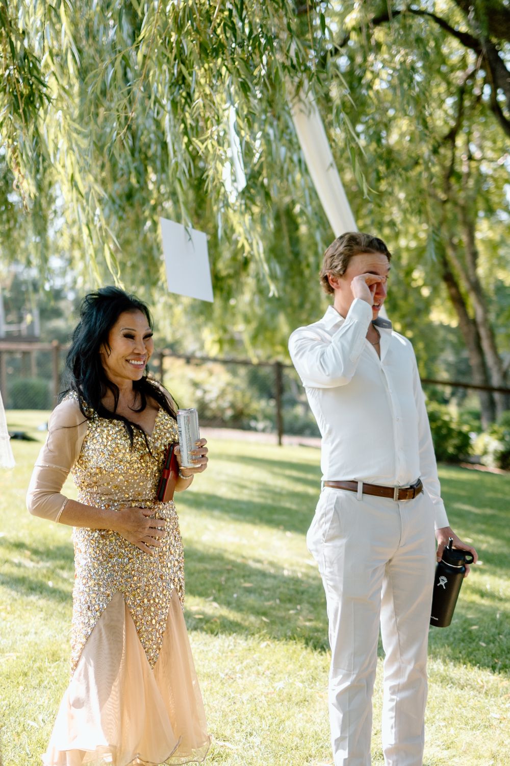 Couple sharing an emotional moment under a willow tree during an outdoor celebration.