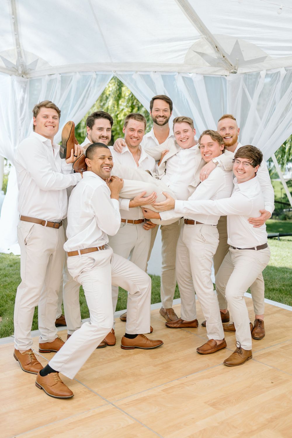 Groomsmen in white shirts and khaki pants posing playfully on wooden dance floor.