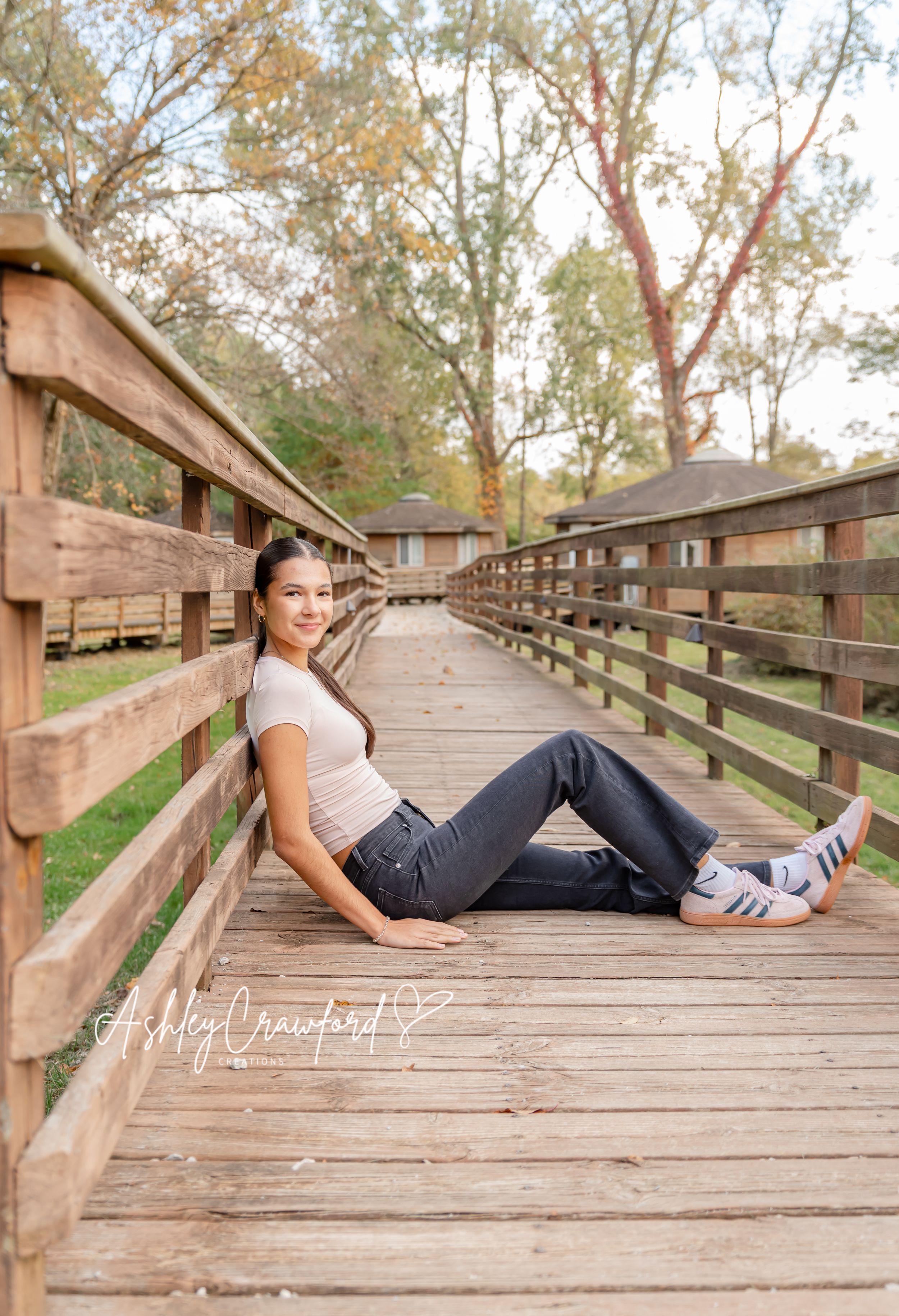 A relaxed portrait on a wooden bridge walkway surrounded by trees.