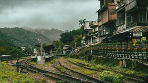 Mountain railway station with curved tracks and traditional buildings nestled in misty green hills.