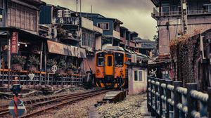 Orange train passing through narrow urban alley surrounded by old residential buildings in Taiwan.