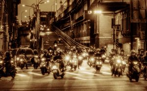 Motorcyclists waiting at a nighttime intersection with glowing headlights on a bustling urban street.
