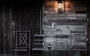 Dark wooden cabin exterior with vintage lantern and chairs creating moody rustic atmosphere.