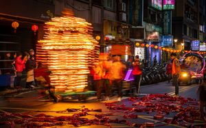 Vendor carrying towering stack of illuminated paper lanterns through bustling night market street.