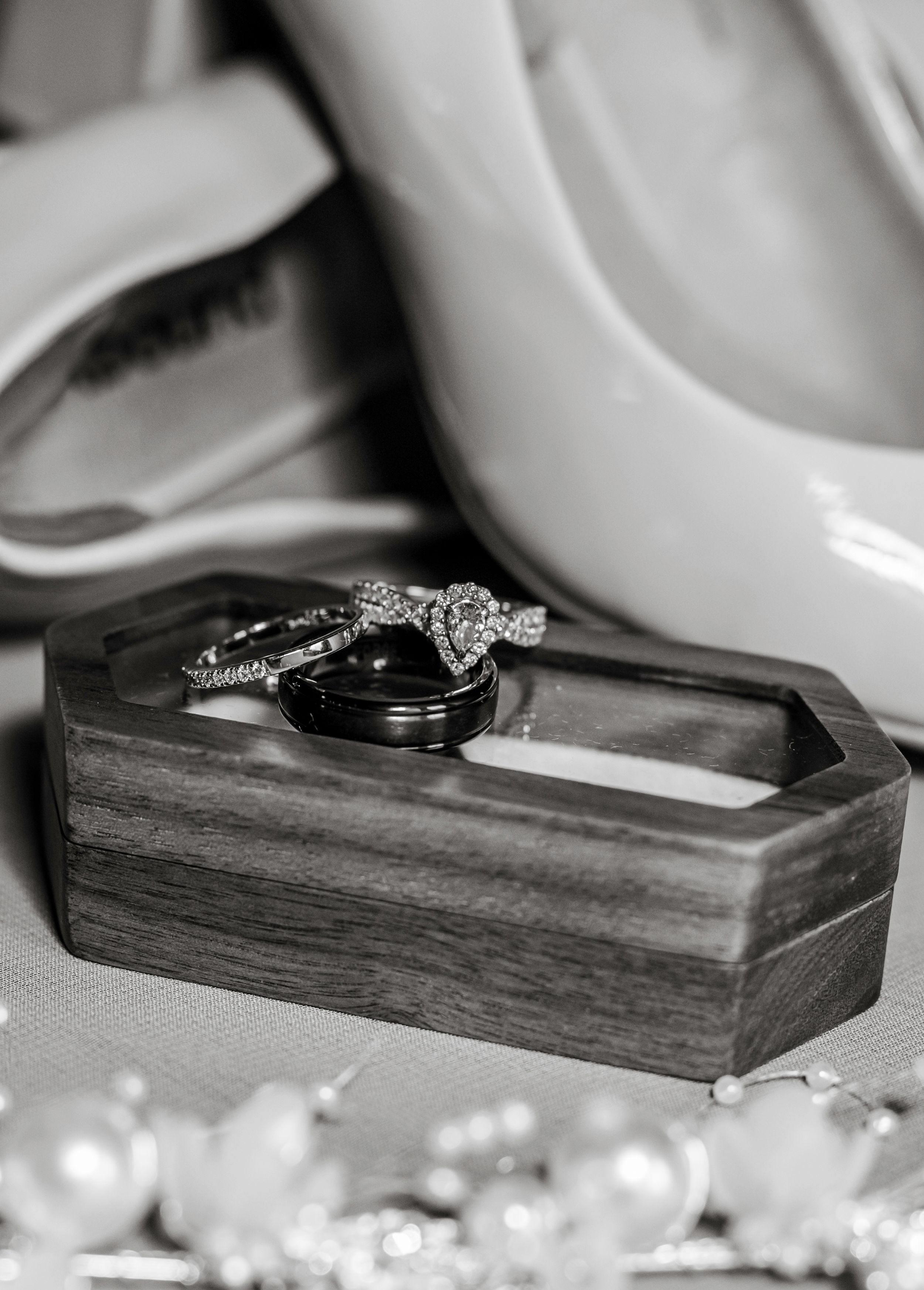 Black and white photo of wedding rings resting on a wooden hexagonal box with delicate details in soft lighting.