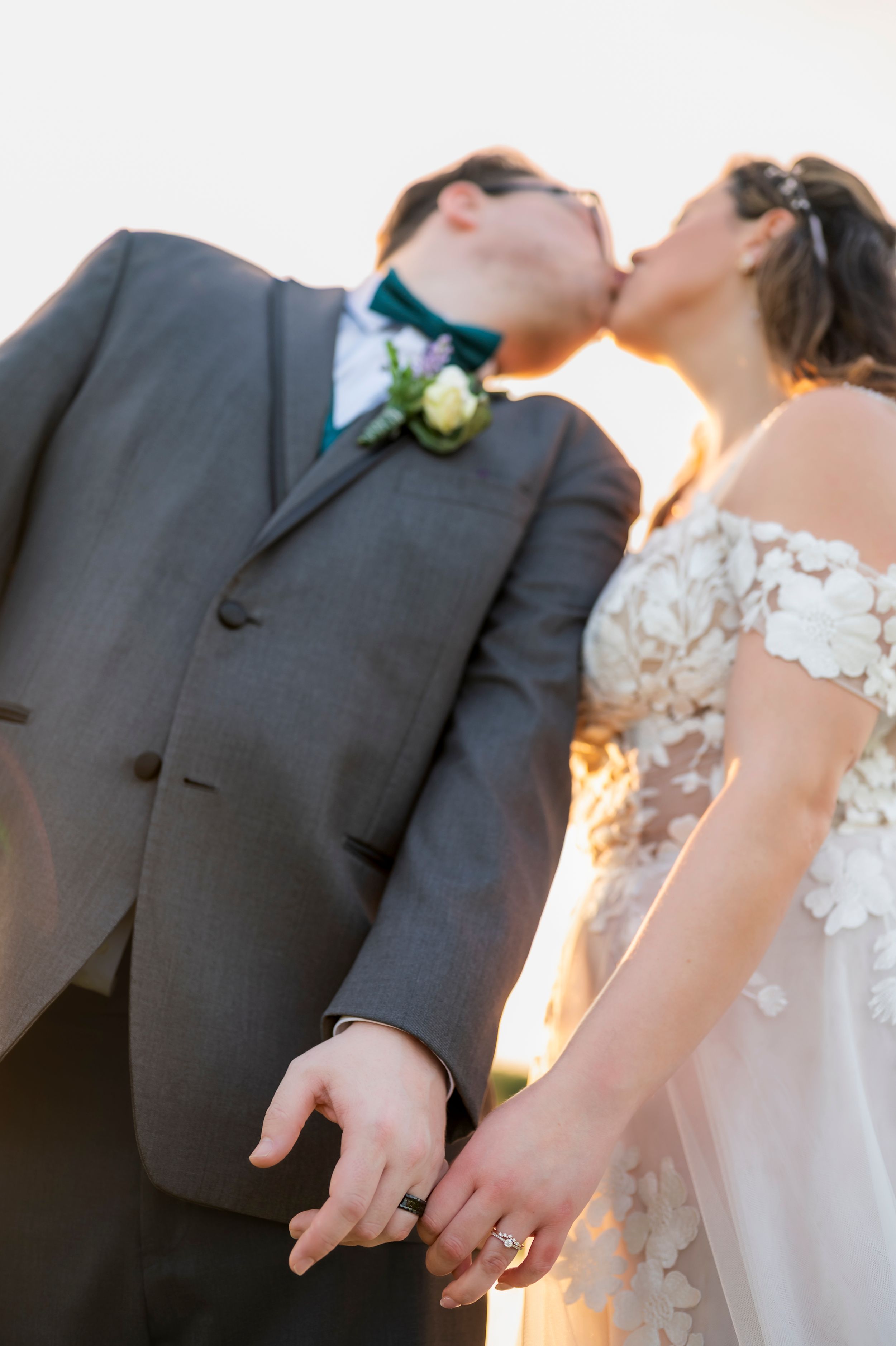Close-up wedding photo details showing hands with rings against formal attire in warm lighting.