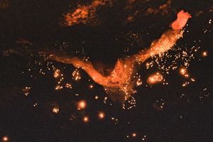 A femme is underwater, colored only in rich amber, surrounded by reflections.