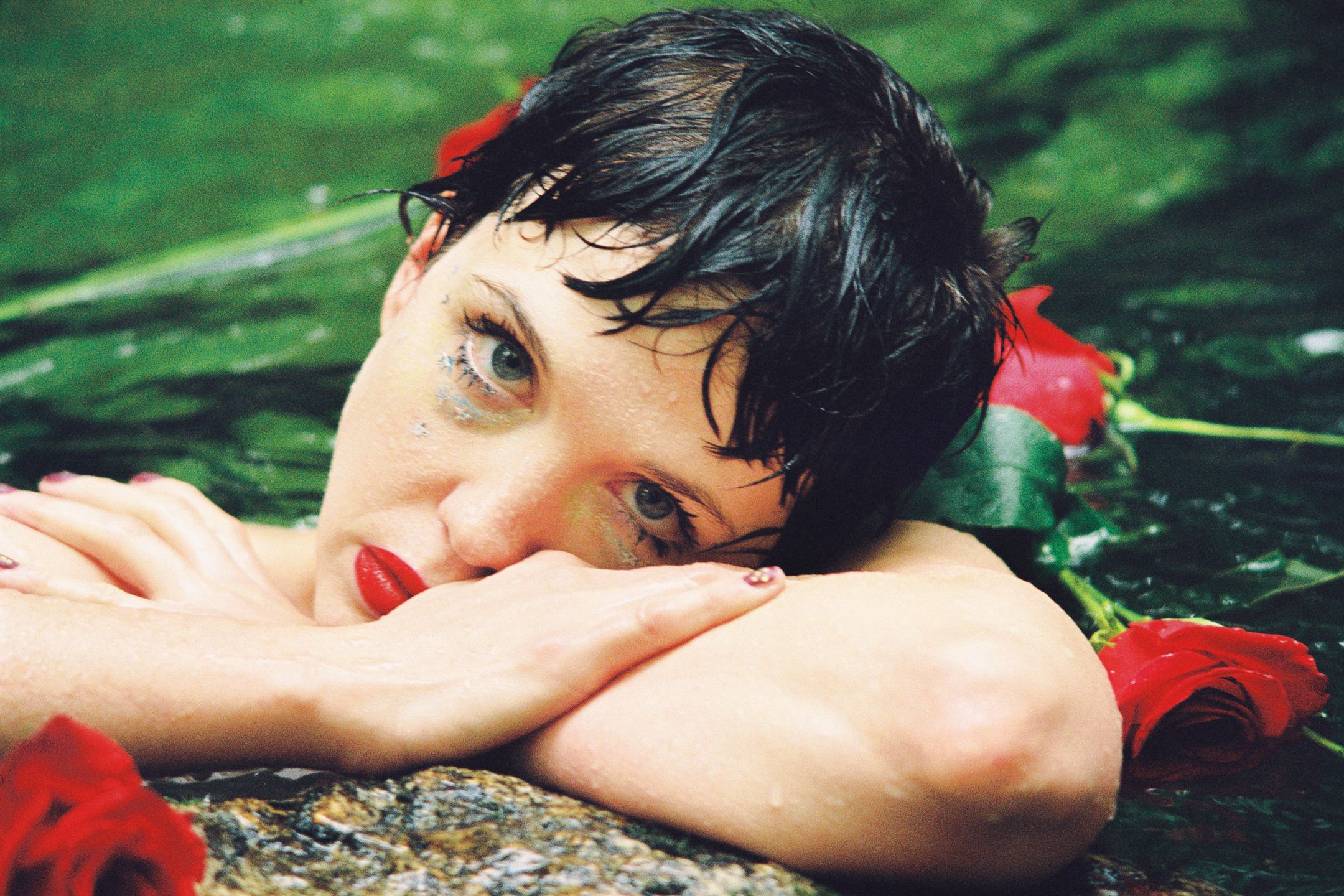 A femme looks at the camera. They are surrounded by roses and green water.