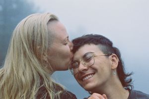 Someone gives their smiling partner a forehead kiss against a misty blue backdrop.