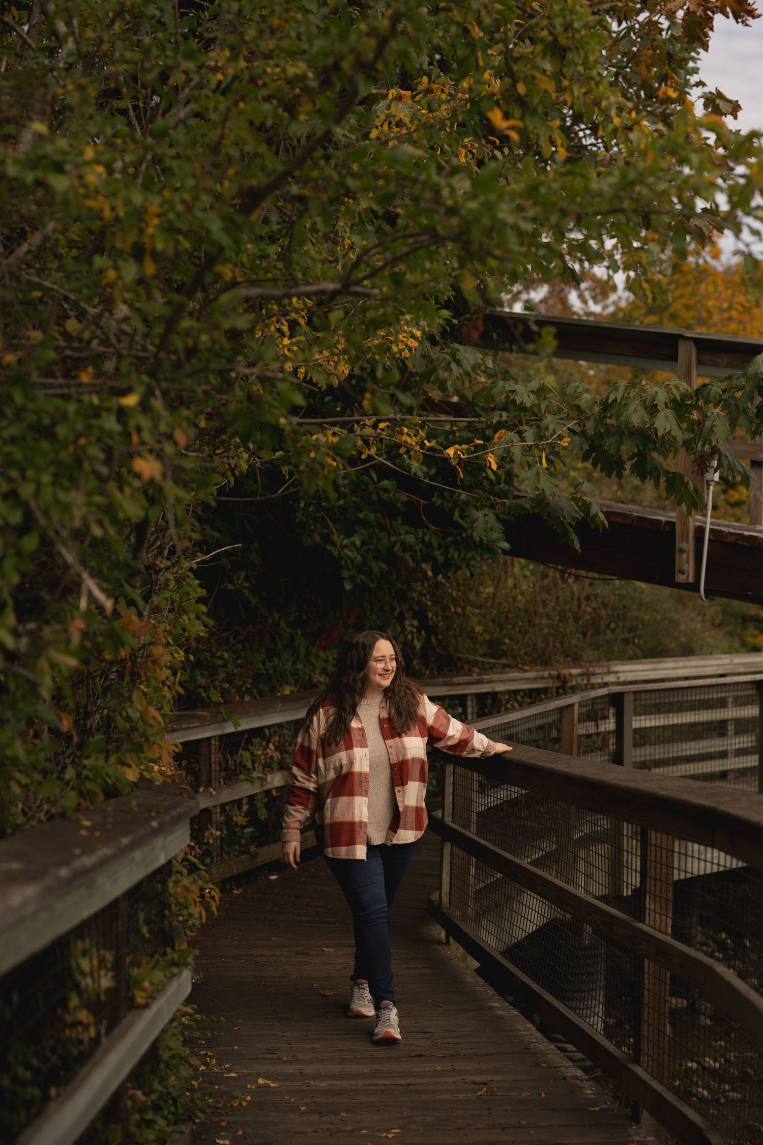 A person in a plaid flannel walks along a wooden boardwalk during autumn.