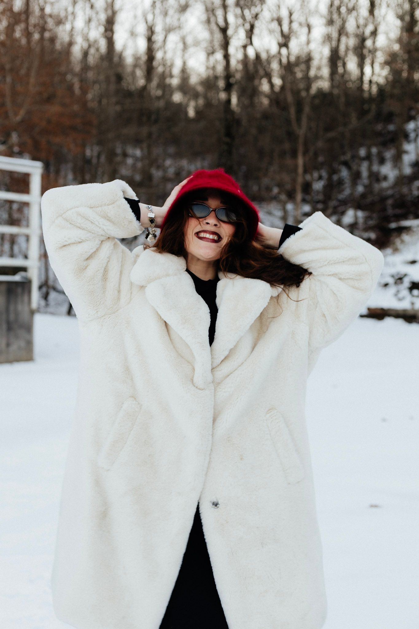 Person in white winter coat playing in snowy landscape with trees in background.
