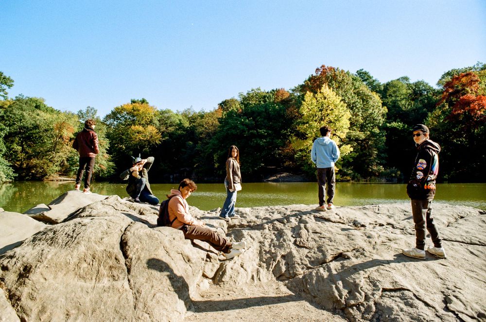Group of people relaxing on rocky outcrop overlooking a lake in Central Park.