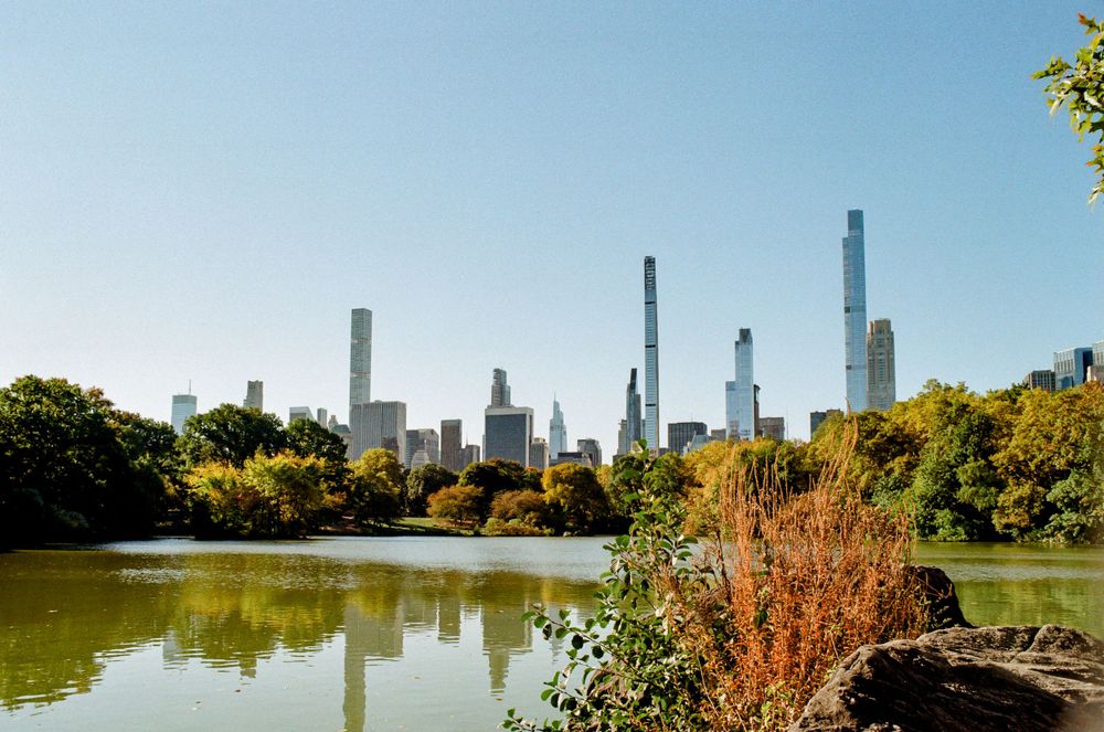 Skyline of Manhattan with tall skyscrapers reflected in Central Park lake during autumn season.