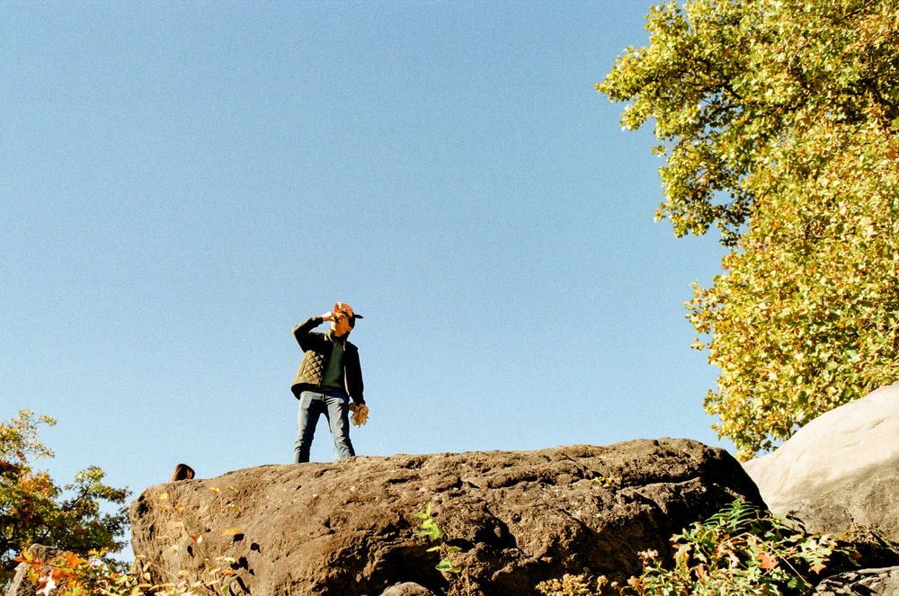 Figure standing on large rock outcrop against bright blue sky and autumn foliage.