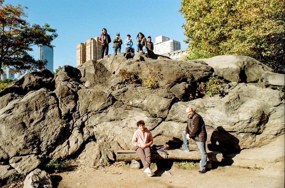 Group gathered on rocky outcrop in Central Park against urban backdrop.