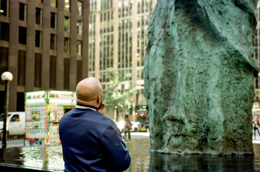 Urban scene showing person viewing bronze sculpture against city buildings.