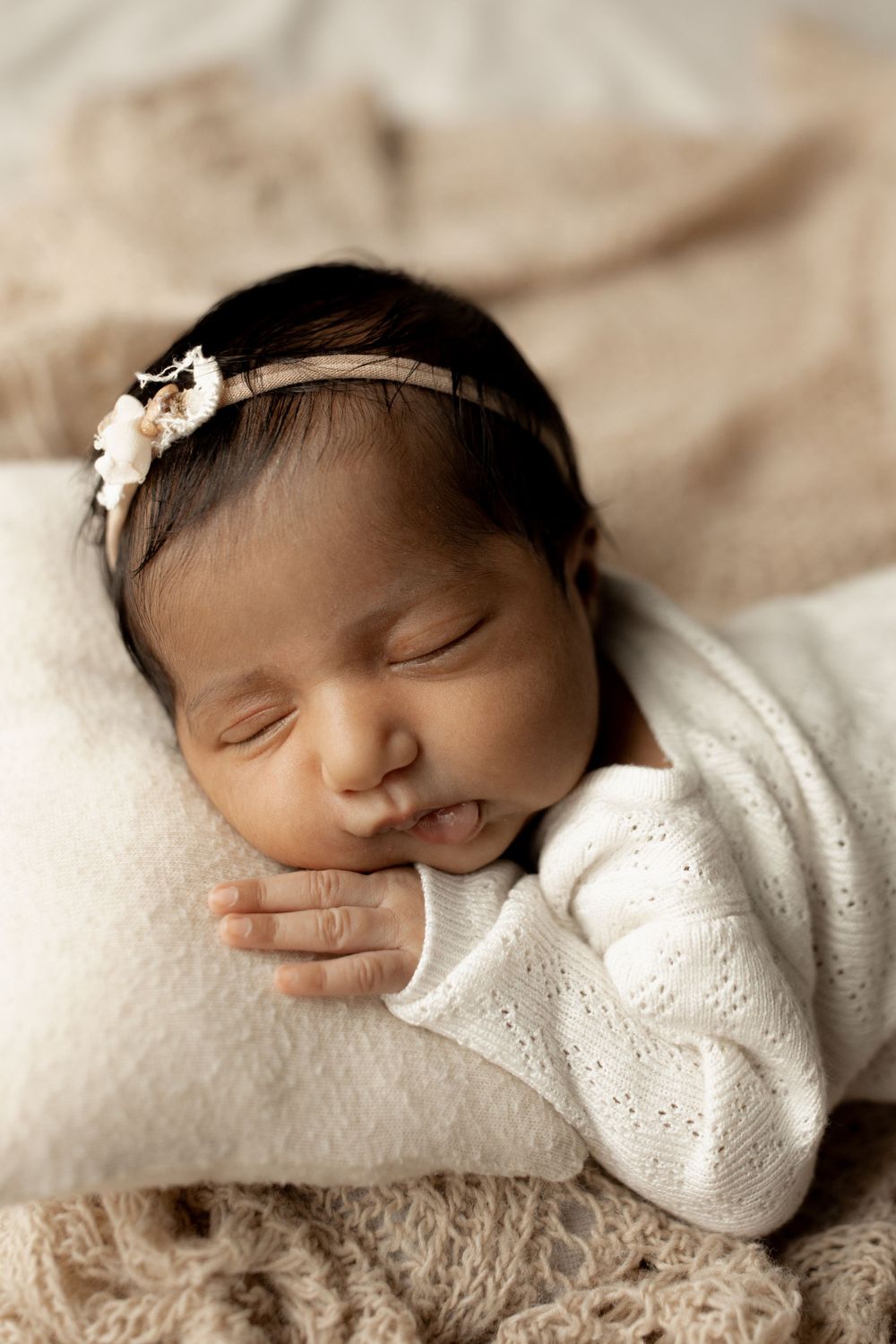 Sleeping newborn baby in white eyelet dress lying on soft beige blanket with delicate floral headband in calgary alberta
