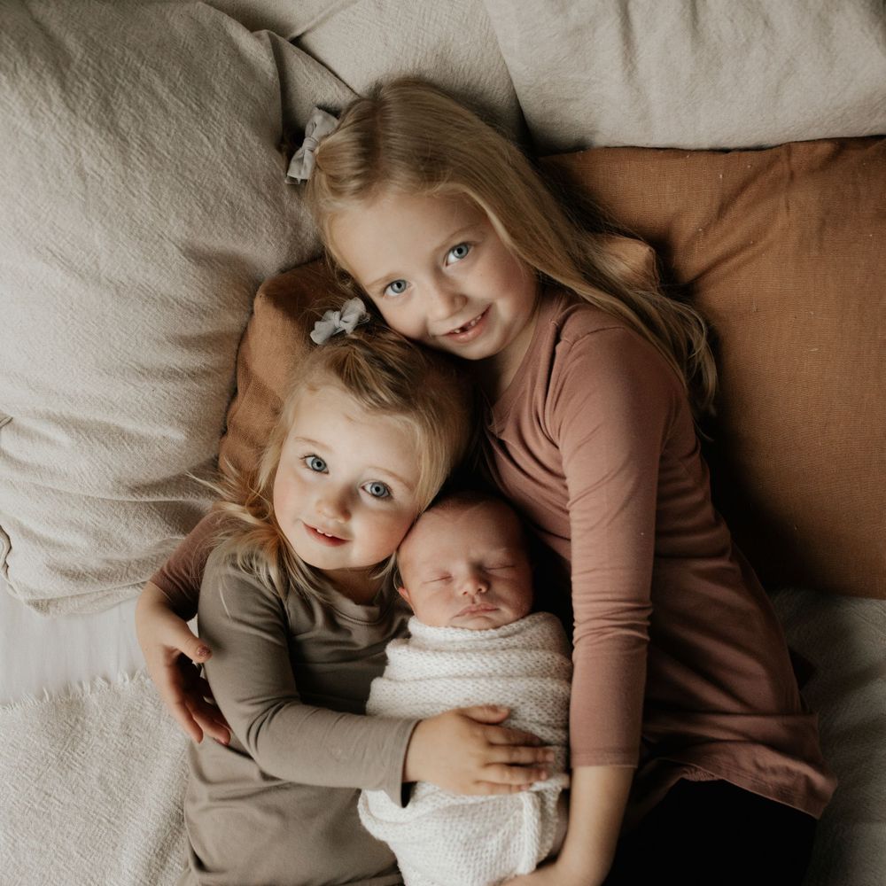 siblings cuddle newborn sister for photoshoot in red deer alberta