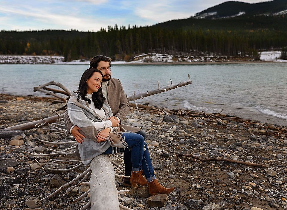 Newly engaged couple sitting on a log at Barrier Lake, Banff Alberta