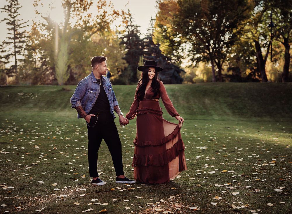 Man wearing jean jacket looking at his girlfriend in long brown dress and black hat at Princes Island Park, Calgary, Alberta