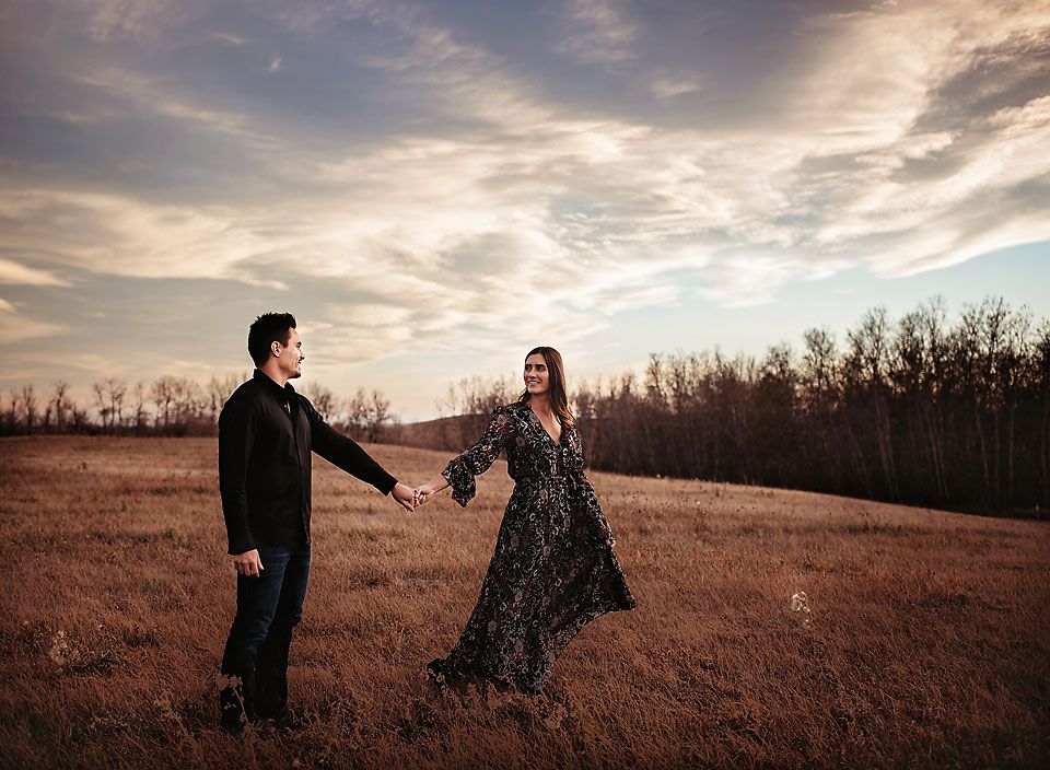 Young man holding young woman's hand at sunset in a field in Airdrie, Alberta