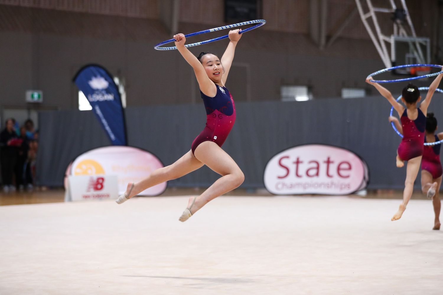 Rhythmic gymnast leaps through the air while performing with clubs at a state competition.