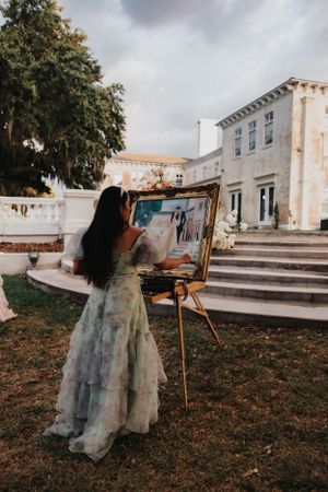 Outdoor painting session with easel set up on grass near classical architecture.