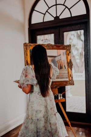 Multiple reflections of a floral dress appear in vintage gold-framed mirrors against white walls.