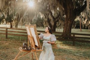 An artist works at an easel under moss-covered oak trees during golden hour.
