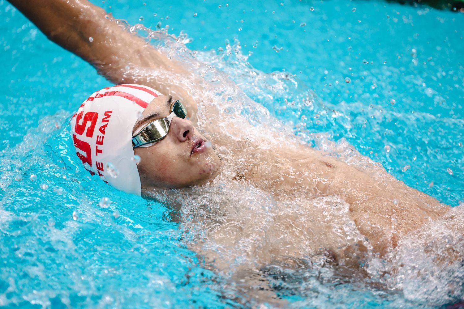 Swimmer performs backstroke during competitive race in blue pool water.