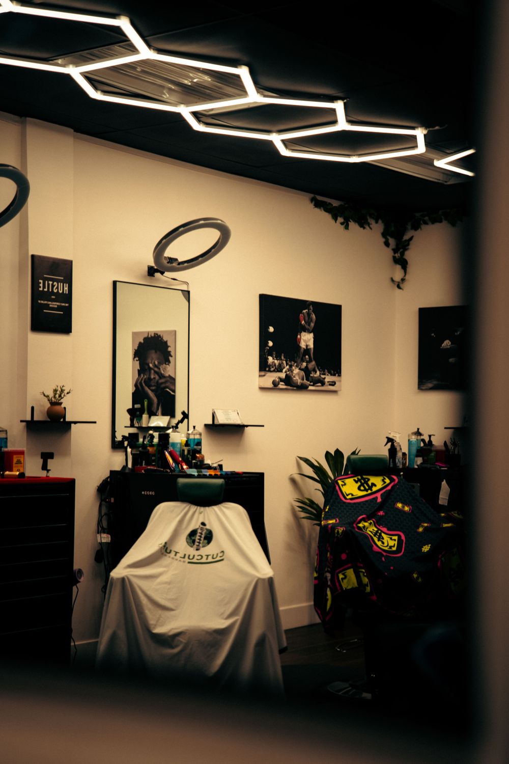 Modern barbershop interior with hexagonal LED ceiling lights, barber chair, and Muhammad Ali poster.