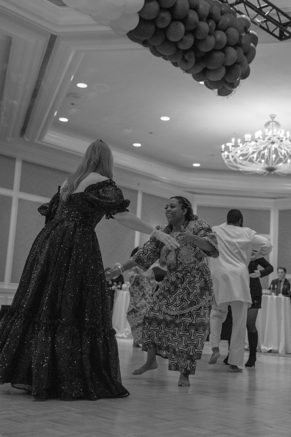 Black and white photo of elegantly dressed women dancing together in a grand ballroom at a formal gala.
