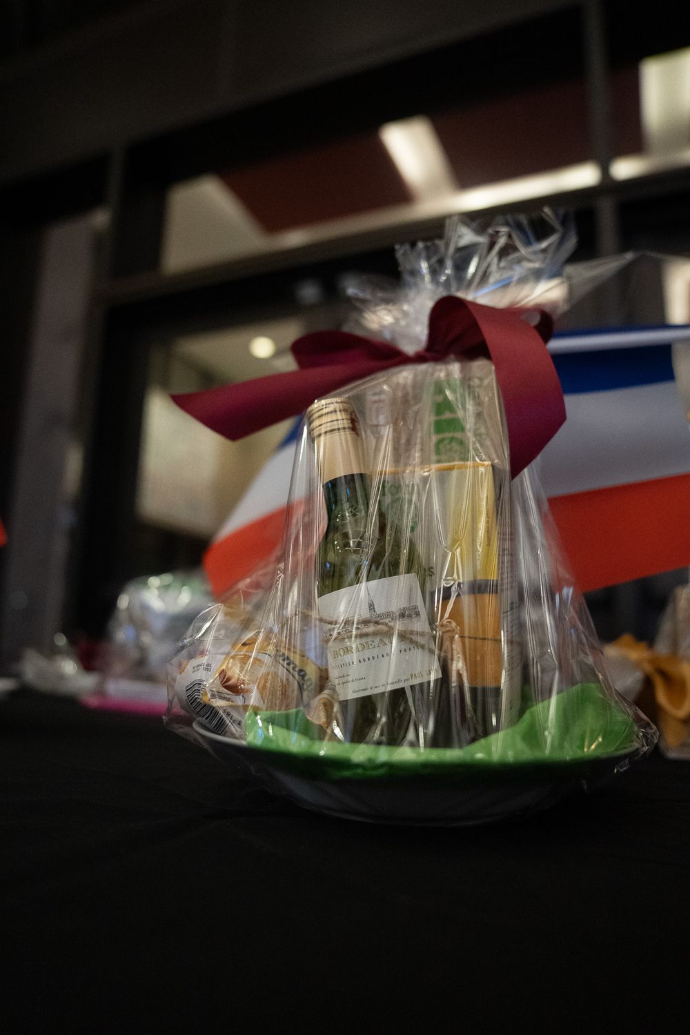 Elegant gift basket with wine bottle wrapped in clear cellophane tied with a burgundy bow at French event.