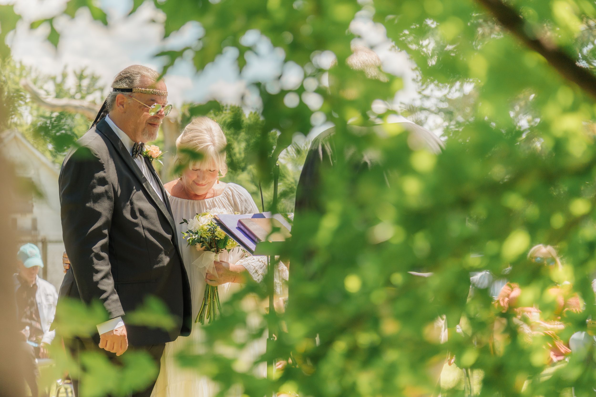 A peak through leaves of the couple at an outdoor wedding ceremony