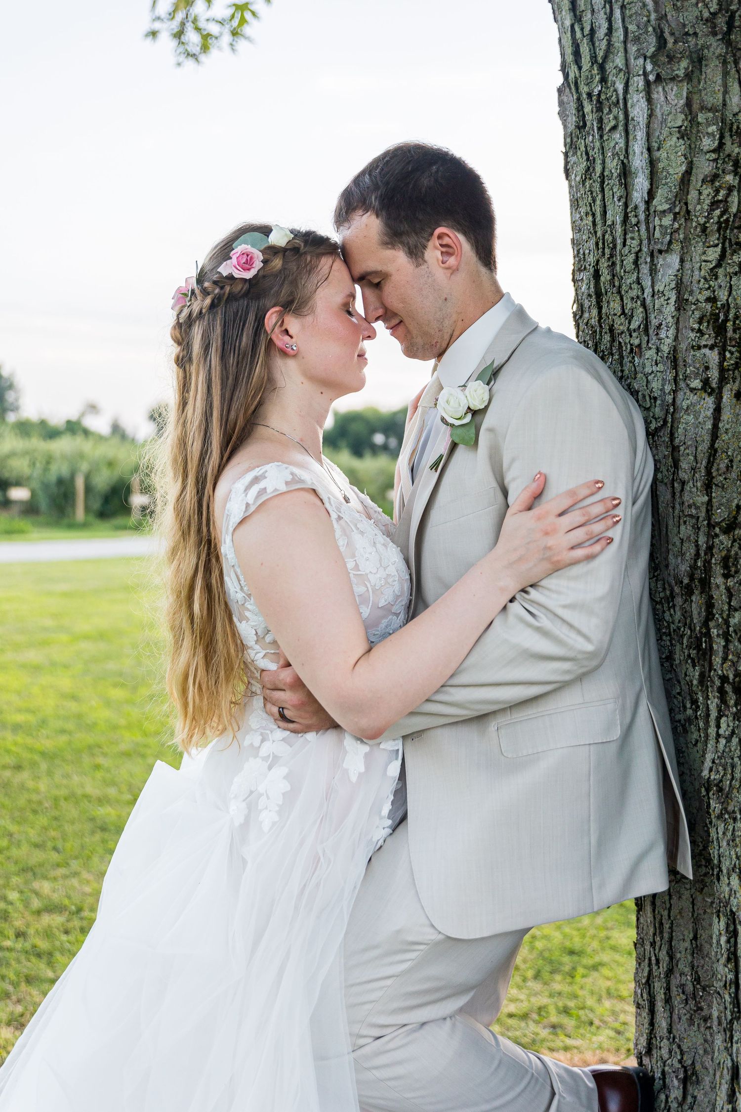 An intimate wedding portrait of a couple posed near a tree trunk in a serene outdoor setting.