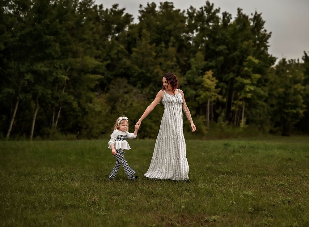 Woman in black and white long dress holding her toddler's hand walking in the forest in Airdrie, Alberta