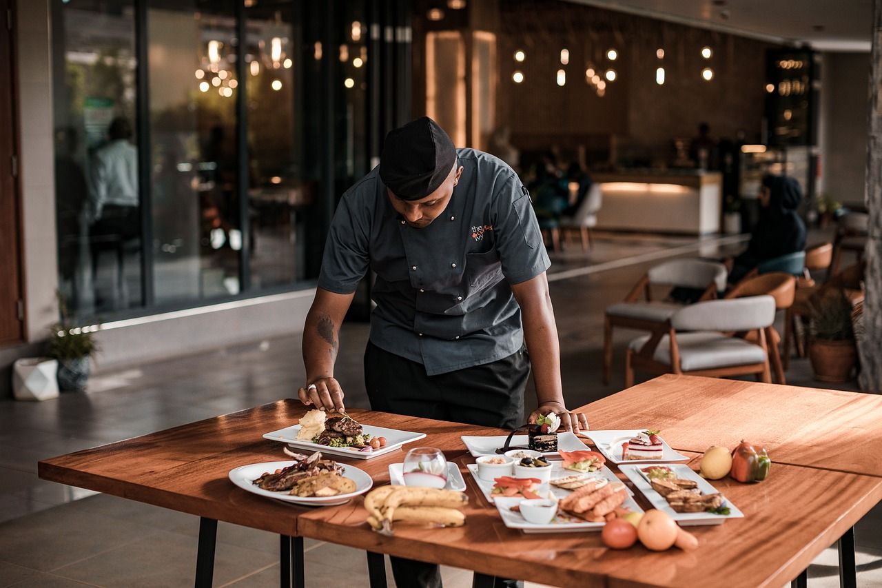Chef preparing food at wooden table in dimly lit restaurant kitchen.
