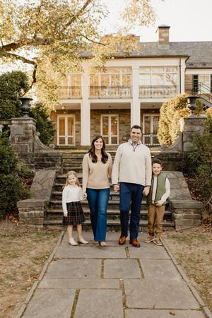 A family stands together on stone steps in front of a stately Southern-style home with white columns at golden hour in Rockville Maryland