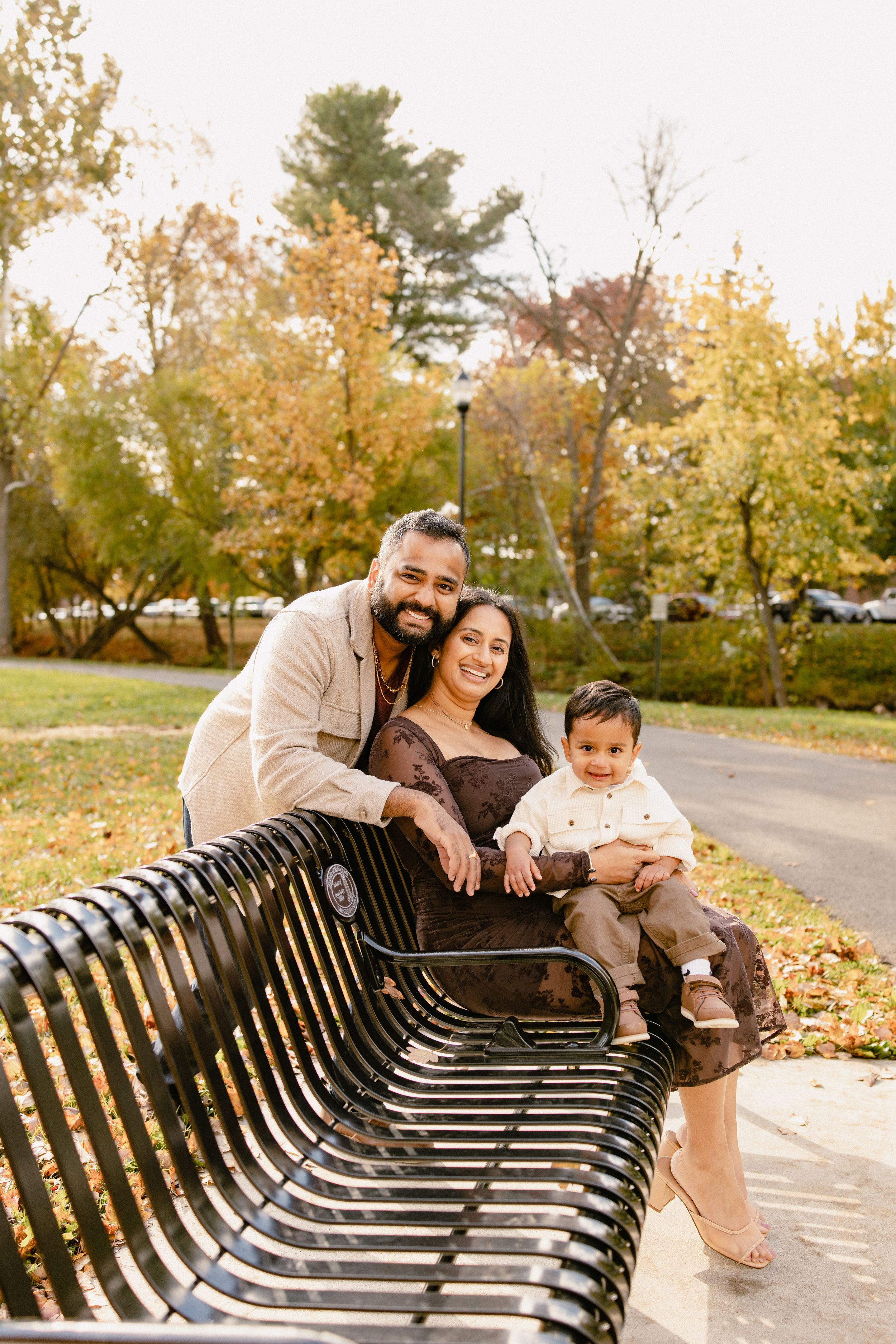Family enjoying autumn day sitting together on curved wooden park bench surrounded by golden fall foliage in Frederick Maryland