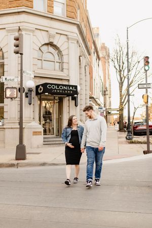A couple walks together and laughs on a city sidewalk near historic brick buildings and storefronts in Frederick Maryland