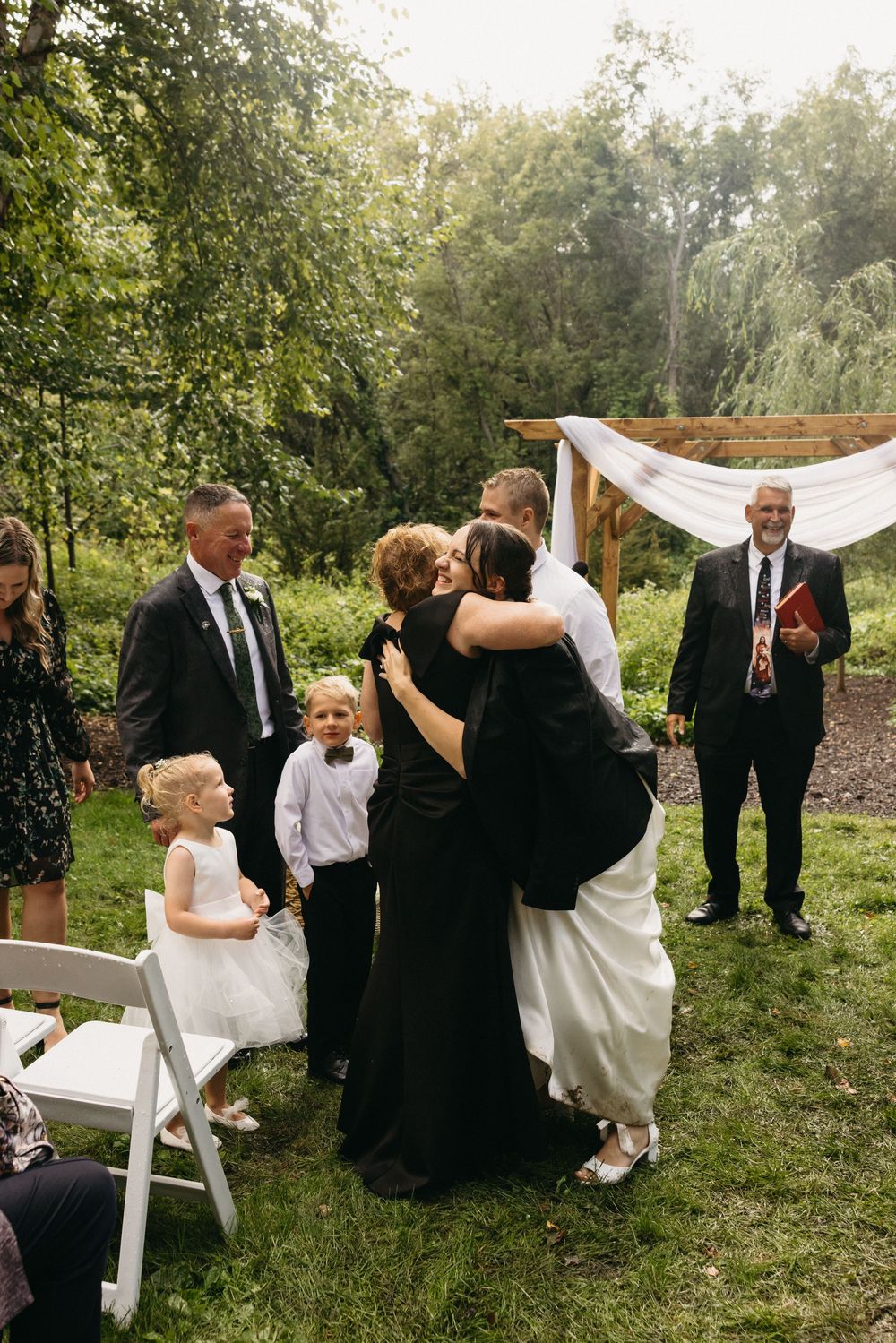 Wedding party playfully poses with white veil in outdoor garden setting during photo session.